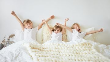 Koncepcja pościeli, snu, odpoczynku i relaksu. Kryty ujęcie trojga dzieci, które czują się senne, budząc się wcześnie rano przed szkołą. Dwóch braci i siostra ziewających i rozciągających się w łóżku
